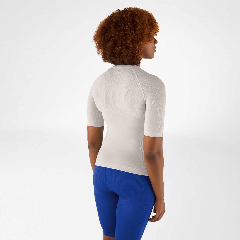 Rückansicht einer Frau mit lockigem Haar in einem athrazit farbenen Kompressionsshirt und blauen Leggings, die leicht zur Seite schaut.