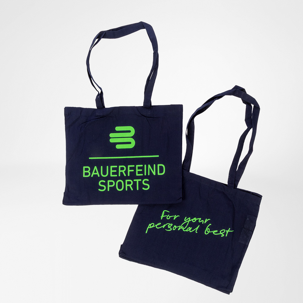 Tragen, was dich weiterbringt – mit Style und Statement Zwei dunkelblaue Baumwolltaschen von Bauerfeind Sports mit neongrüner Aufschrift. Eine Tasche zeigt das Bauerfeind-Sports-Logo, die andere den Slogan „For your personal best“.