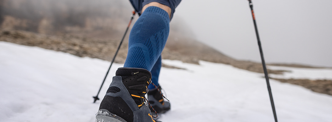 Merino-Wandersocken hellblau beim Wandern Person wandert über Schnee-bedeckte-Felsen sie trägt Merino-Wandersocken
