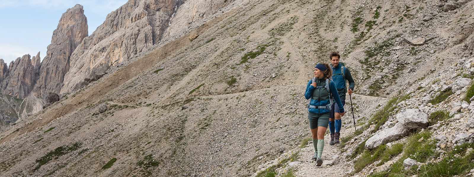 Merino Wandersocken: Dein Begleiter auf der nächsten Wandertour Mann und Frau wandern mit Wanderstöcken in der Hand einen Berg hinab und tragen dabei Wandersocken