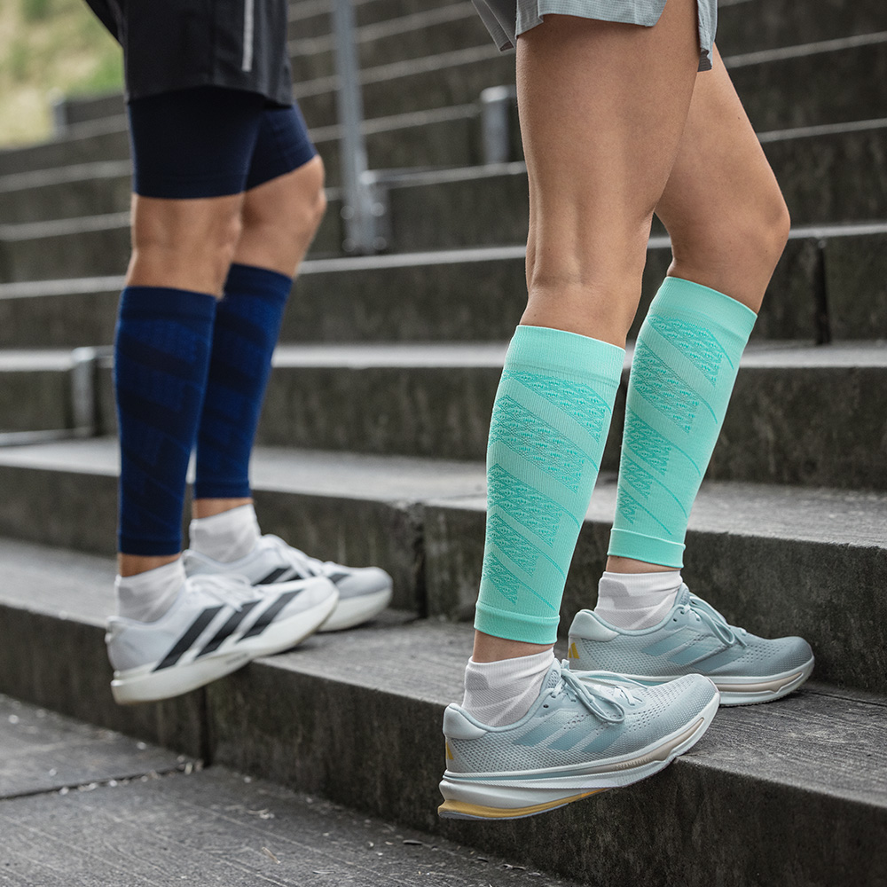 Zwei Läufer beim Treppentraining im Freien. Sie tragen Run Performance Sleeves mit Kompression in Mint und Navy, die die Waden stabilisieren und die Durchblutung fördern.