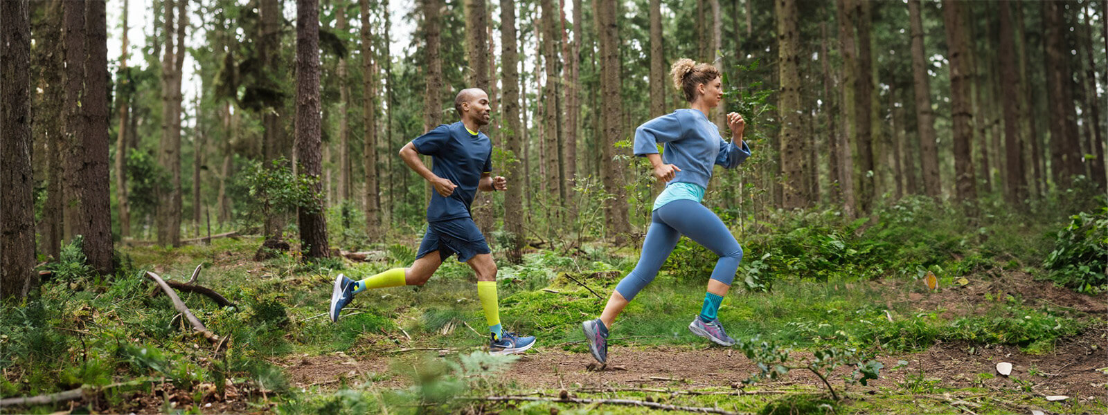 Eine Frau und ein Mann rennen durch einen dichten Wald und tragen Bandagen