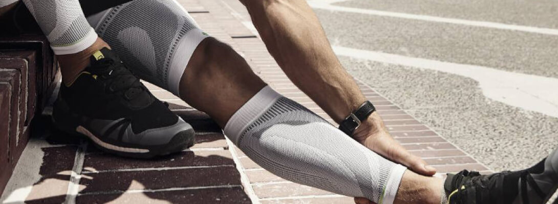 Waden Sleeves beim Sport Auf Stufen sitzender Läufer der weiße Lower Leg und Upper Leg Sleeves trägt faßt sich an sein Bein
