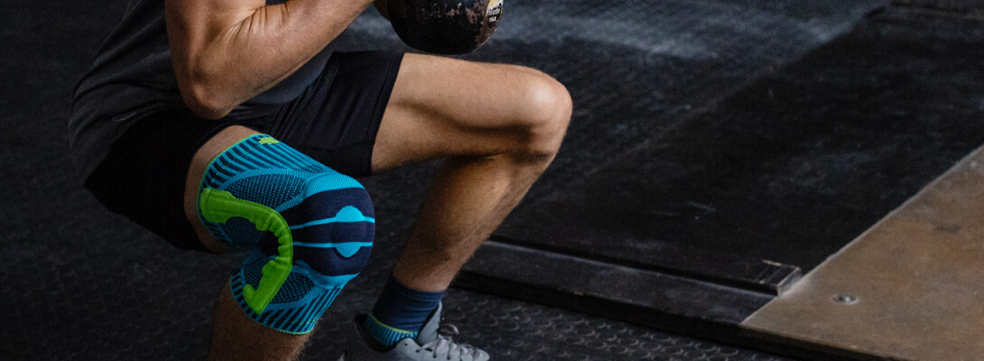 Sportler im Fitnessstudio in der Kniebeuge trägt eine Kniebandage für den Sport