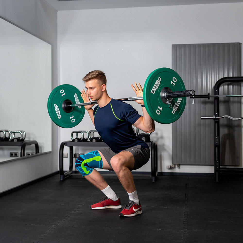 Mann im Fitnessstudio mit Kniebandage macht einen Squat mit einer Langhantel auf dem Rücken