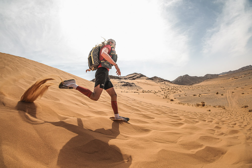 Ultrarunner beim Laufen durch Sanddünen in einer kargen Wüstenlandschaft