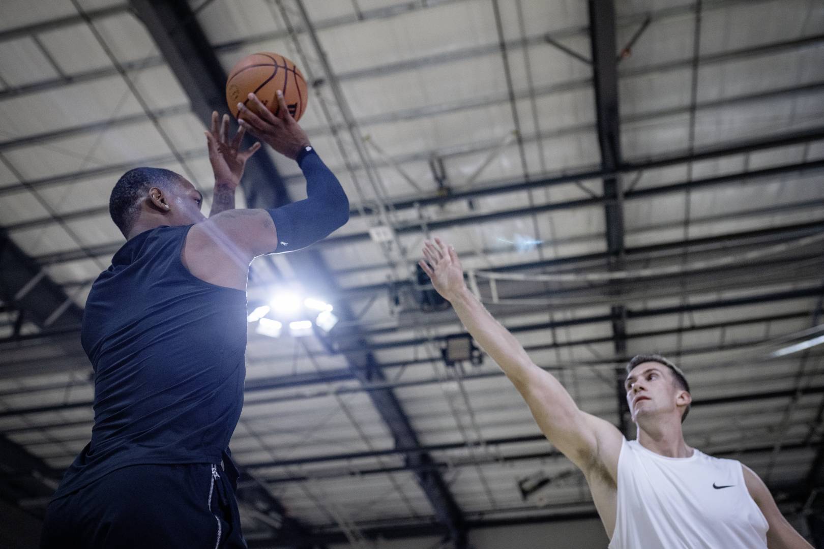 Basketballer mit blauem Armsleeve in Sporthalle versucht über den ausgestreckten Arm eines Gegenspielers zu werfen