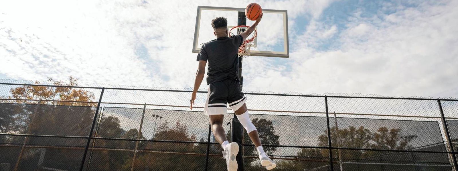 Basketballspieler springt auf einem Freiplatz zum Korb und trägt dabei eine weiße Kniebandage