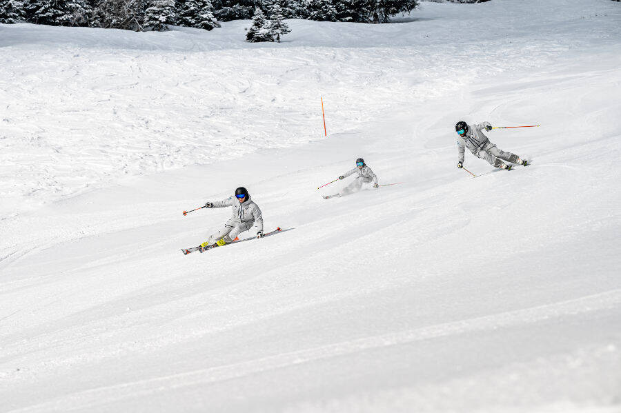 Drei grau gekleidete Skifahrer bei einer gemeinsamen Abfahrt seitlich hintereinander versetzt und in schrägen Fahrpositionen