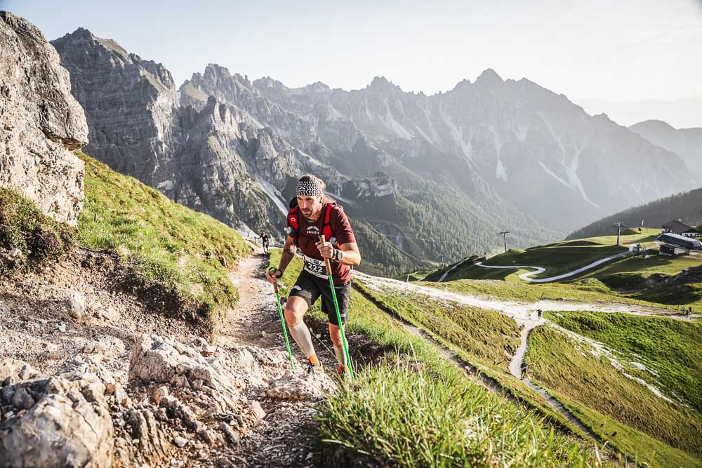 Ultrarunner beim steilen Aufstieg mit Laufstöcken auf einem alpinen Bergtrail