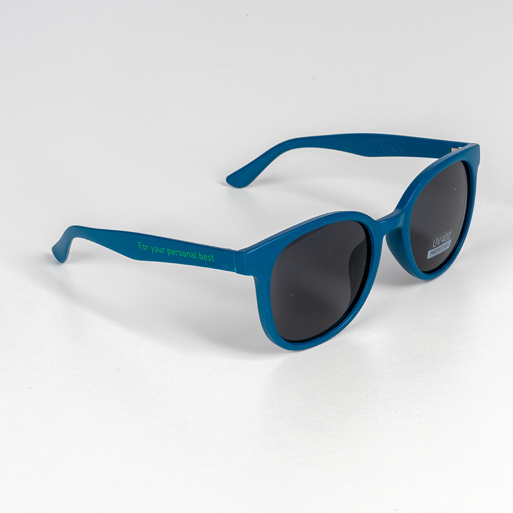 Für klare Sicht auf dein Ziel – mit UV-Schutz und Attitude. Blaugrüne Sonnenbrille mit dunklen Gläsern und dem grünen Aufdruck „For your personal best“ auf dem Bügel. Die Brille liegt auf weißem Hintergrund.