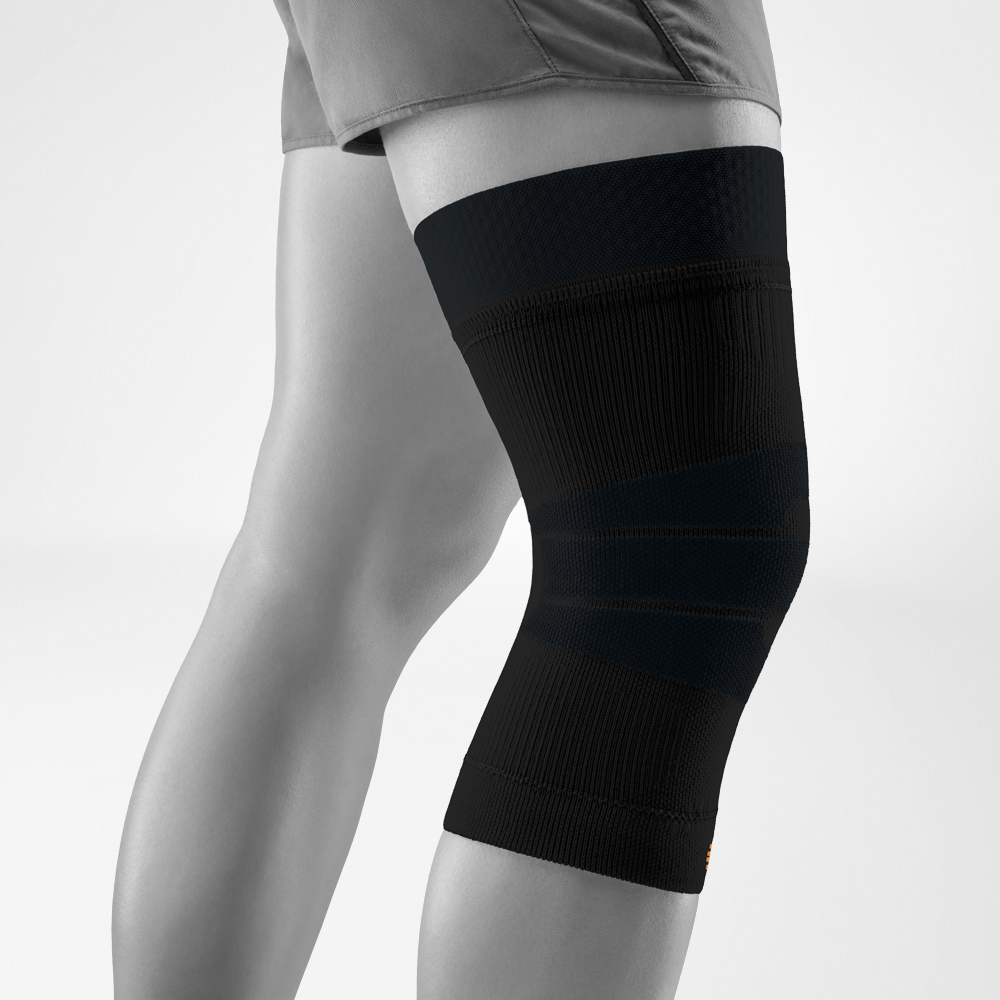 Schwarze Kniebandage für Outdoor-Aktivitäten, seitlich am Bein getragen. Das elastische Gestrick stabilisiert das Kniegelenk, während die Kompression die Durchblutung fördert und Bewegung im Freien unterstützt.