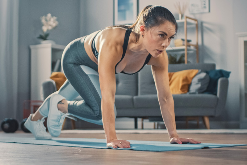Krafttraining für Läufer: Ein paar Minuten zwischendurch reichen vollkommen aus Frau macht Mountain Climbers im Wohnzimmer im Hintergrund eine Couch und Regale