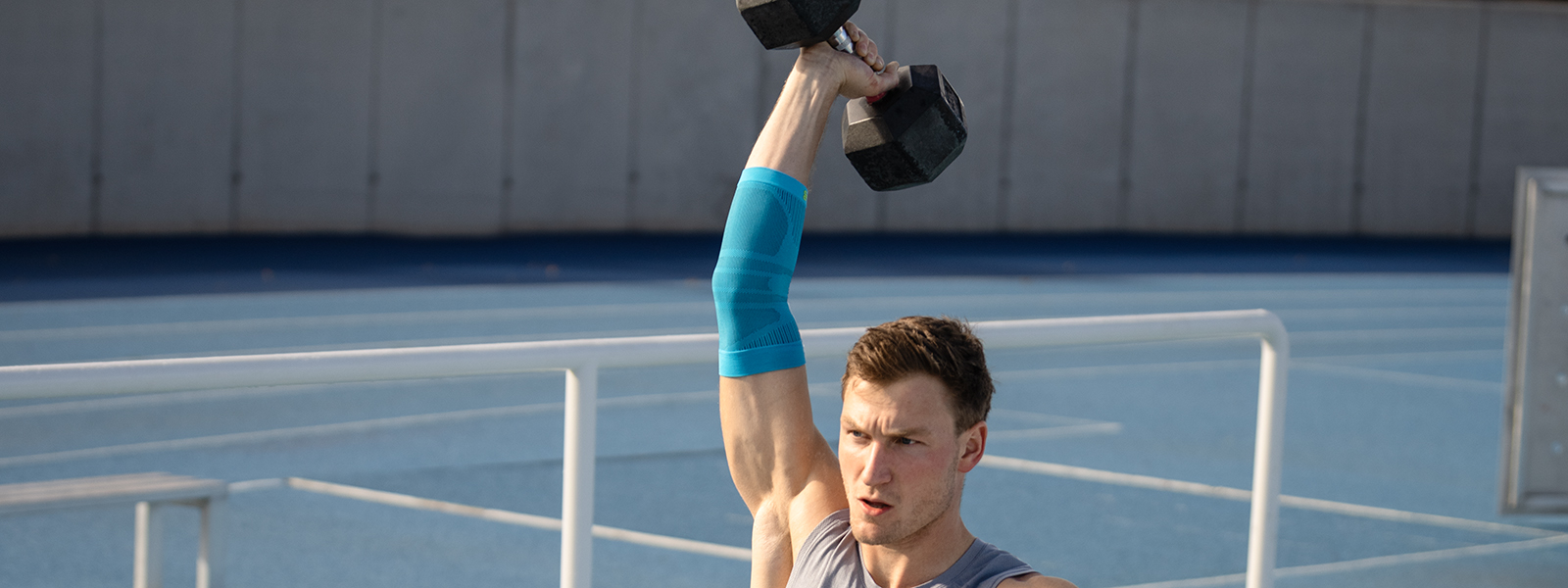 Ellenbogenbandage beim Fitness-Training Thoms Röhler hält ein Gewicht hoch und stabilisiert sein Arm mithilfe einer Ellenbogenbandage