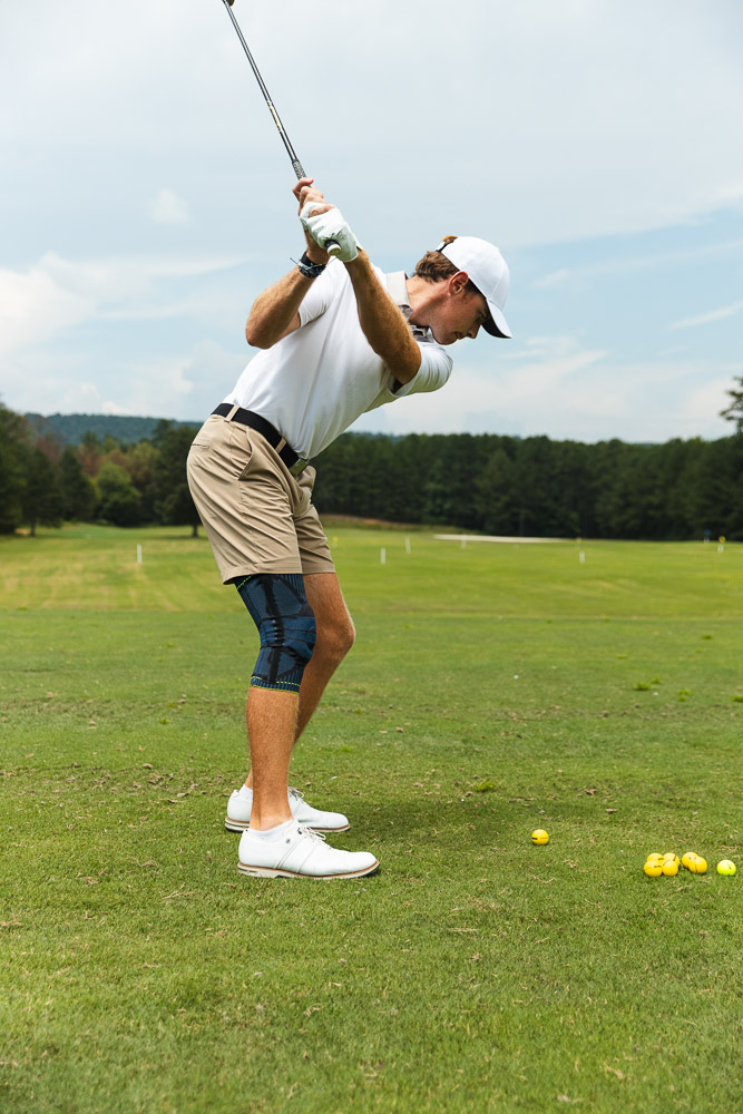 Golfer beim Abschlag auf dem Golfplatz mit Kniebandage für Stabilität und Unterstützung im Schwung.