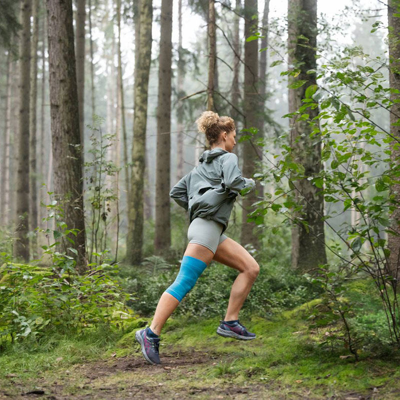 Eine Läuferin mit Knie Bandage rennt durch einen dichten Wald