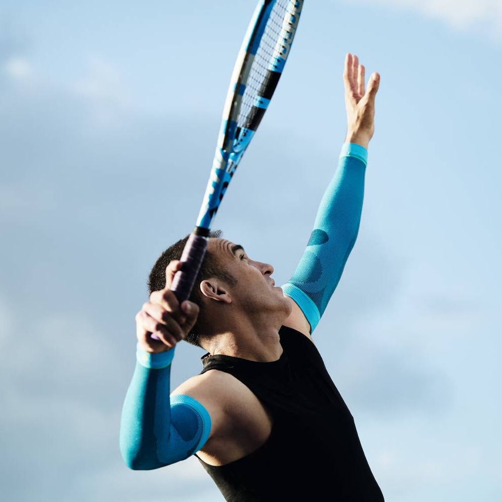 Tennisspieler mit blauen Kompressionsärmeln beim Aufschlag Ein Tennisspieler mit blauen Kompressionsärmeln beim Aufschlag. Der Himmel ist blau mit wenigen Wolken.