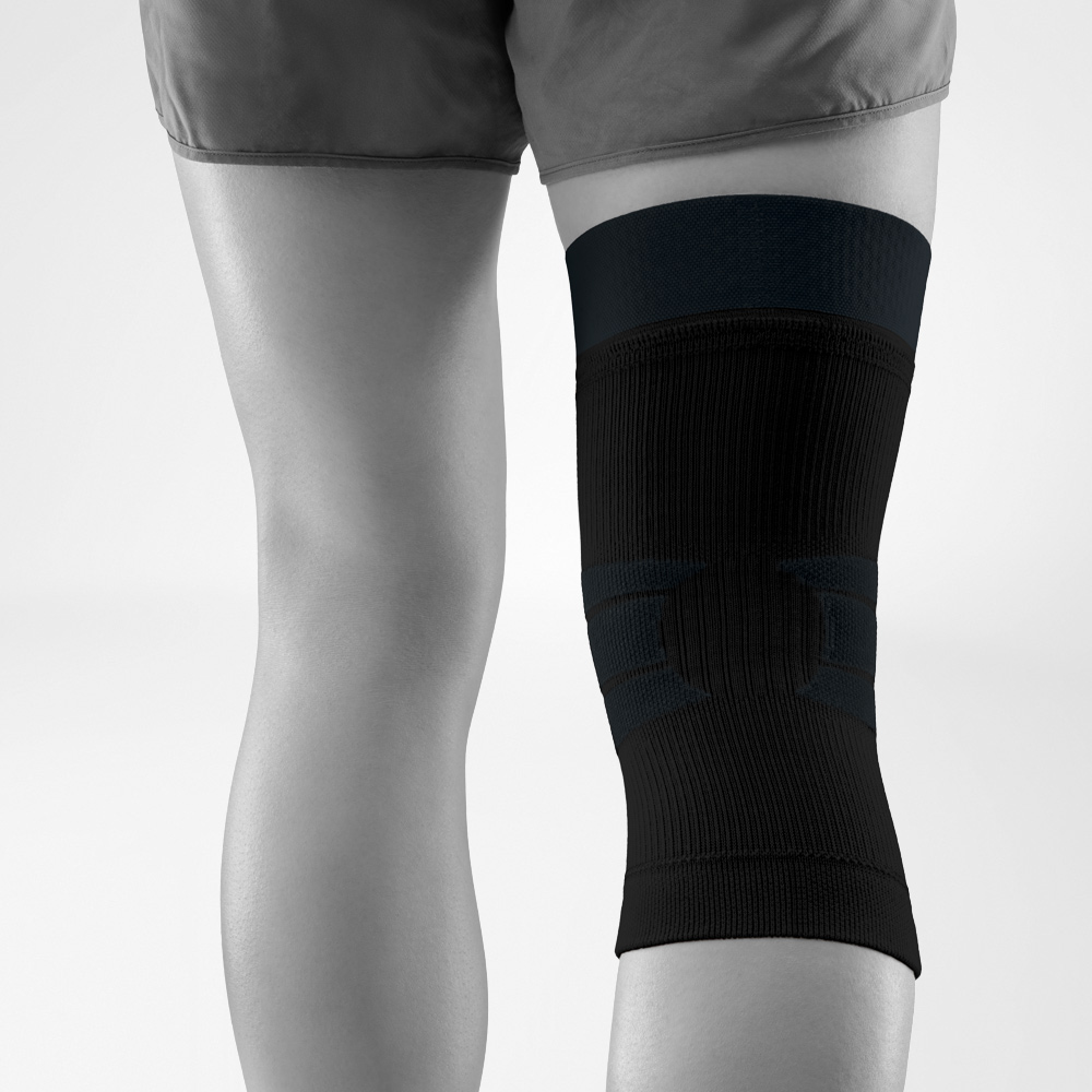 Rückansicht einer getragenen schwarzen Kniebandage. Das anatomische Strickdesign mit integrierter Stabilisierung umschließt das Knie sicher und sorgt für Bewegungsfreiheit bei Outdoor-Aktivitäten.
