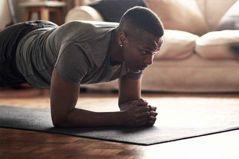 Krafttraining für Läufer: Der Plank als Wohnzimmer-Übung vorm Fernseher Mann macht Plank im Wohnzimmer im Hintergrund eine helle Couch