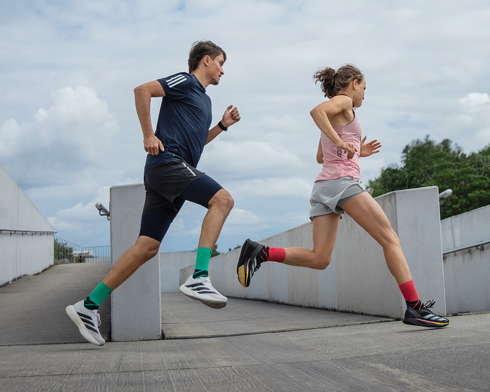 Noch stärker im Team: Eine Marathonvorbereitung mit Laufpartnern motiviert ganz besonders Gruppe aus drei Läufern läuft um eine Ecke in einer Altstadt mit Graffitis an den Wänden auf eine Treppe zu