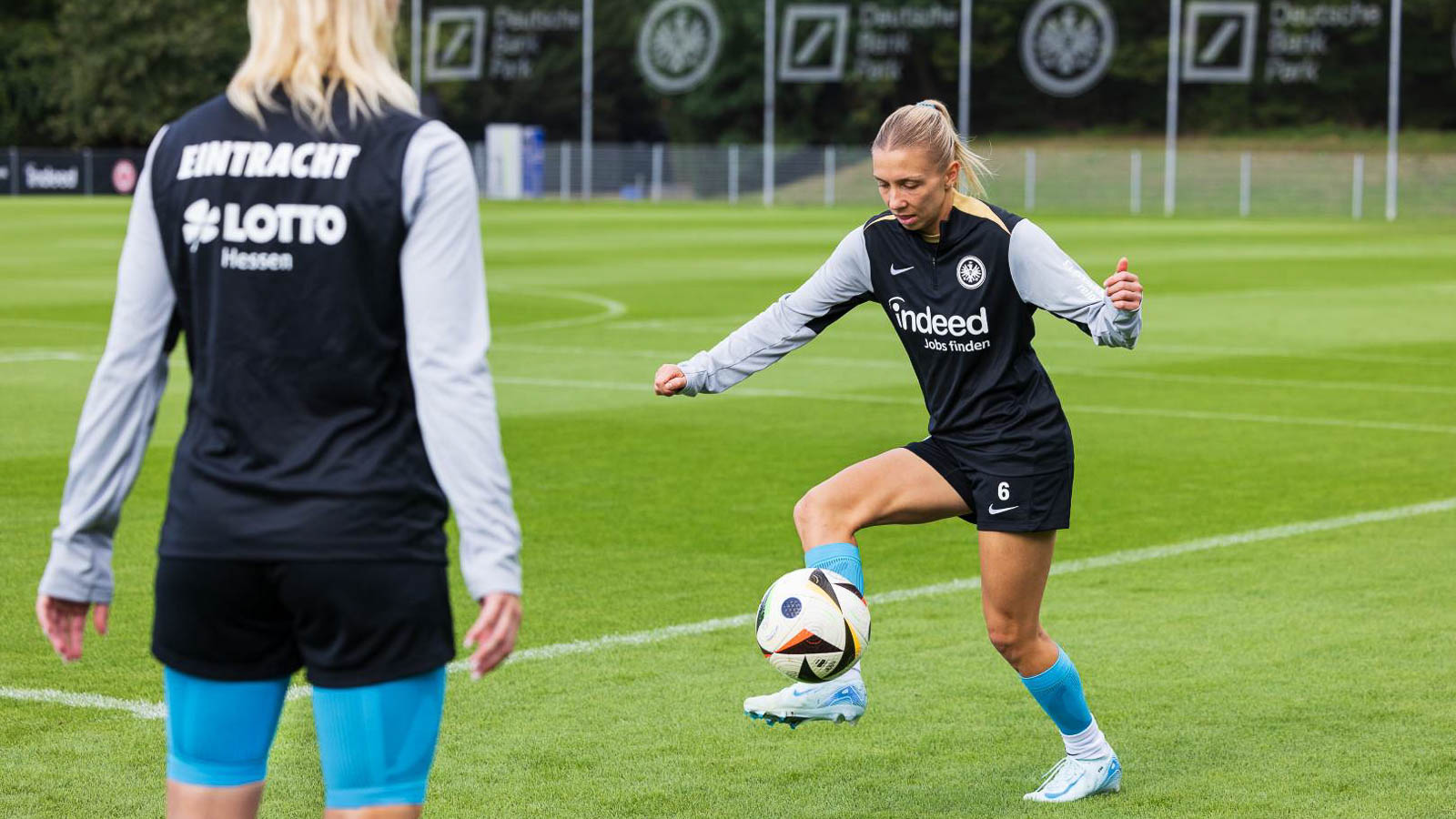 Ballkontrolle und Techniktraining bei Eintracht Frankfurt Eintracht-Frankfurt-Spielerin in Aktion, wie sie den Ball kontrolliert. Im Hintergrund ein weiteres Teammitglied, die das Training beobachtet. Fokus auf Technik und Präzision.