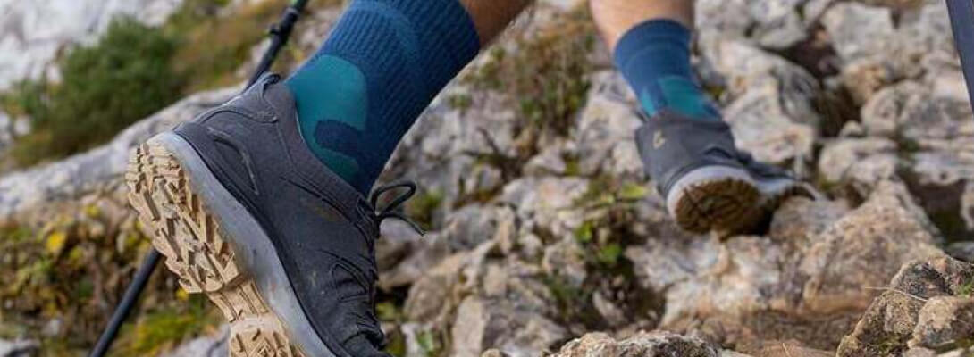 Mittellange Merino-Wandersocken beim Bergsteigen Person wandert über Steine einen Berg hoch und trägt mittellange Wandersocken