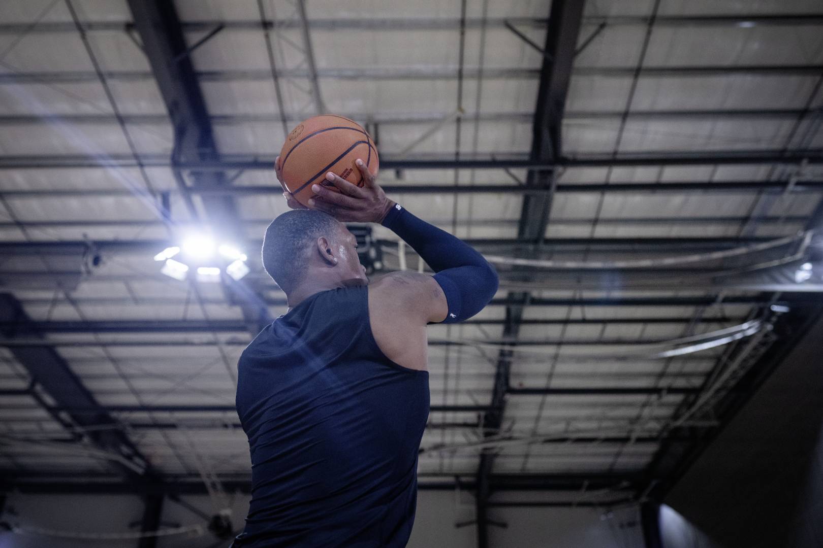 Basketballer mit blauem Armsleeve in Sporthalle setzt mit den Händen oberhalb des Kopfes zum Wurf an