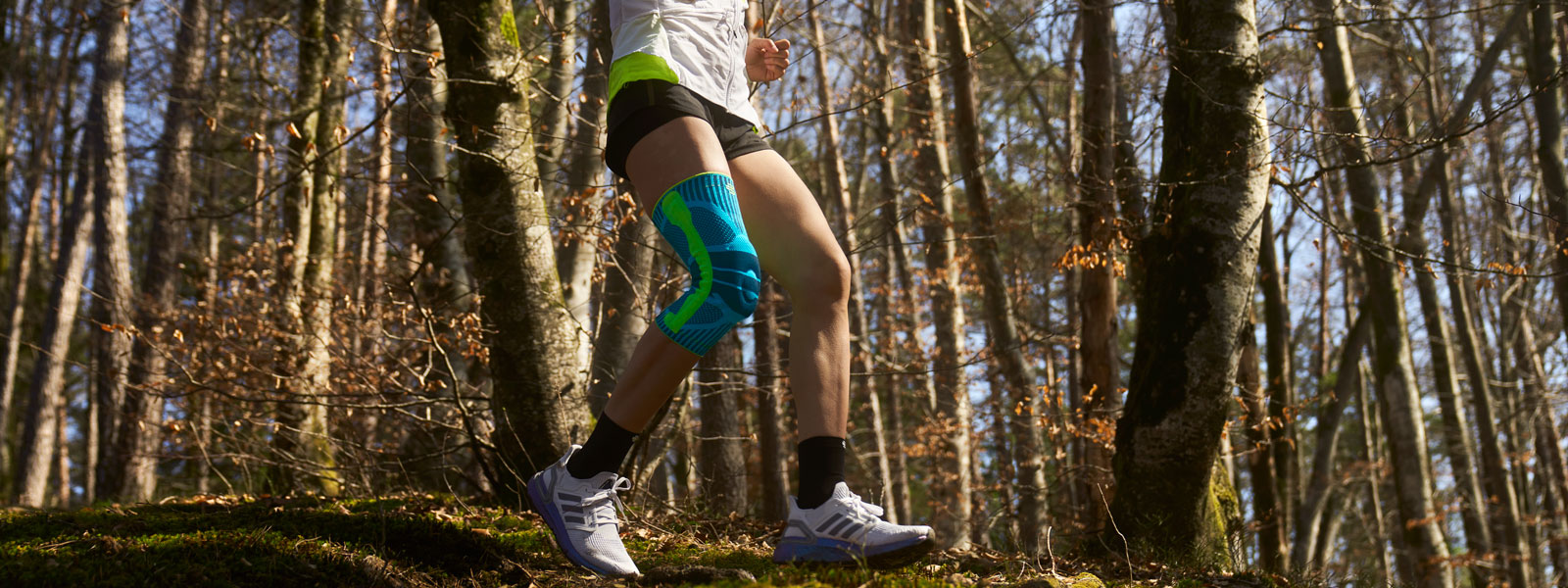 Schmerzreduktion durch die Sports Knee Support beim Lauf über unebenes Gelände Anna Hahner läuft mit einer Kniebandage den Waldweg herunter