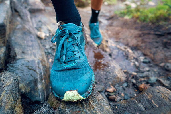 Nahaufnahme eines blauer Laufschuhs auf einem nassen Felsvorsprung