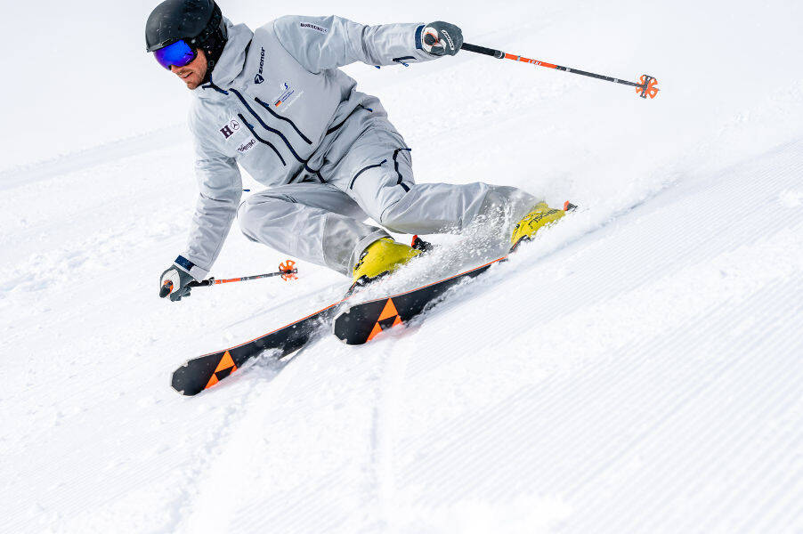 Skifahrer in grauem Anzug mit leichter Schräglage	 vor ihm ist das Rillenmuster der präperierten Piste zu erkennen