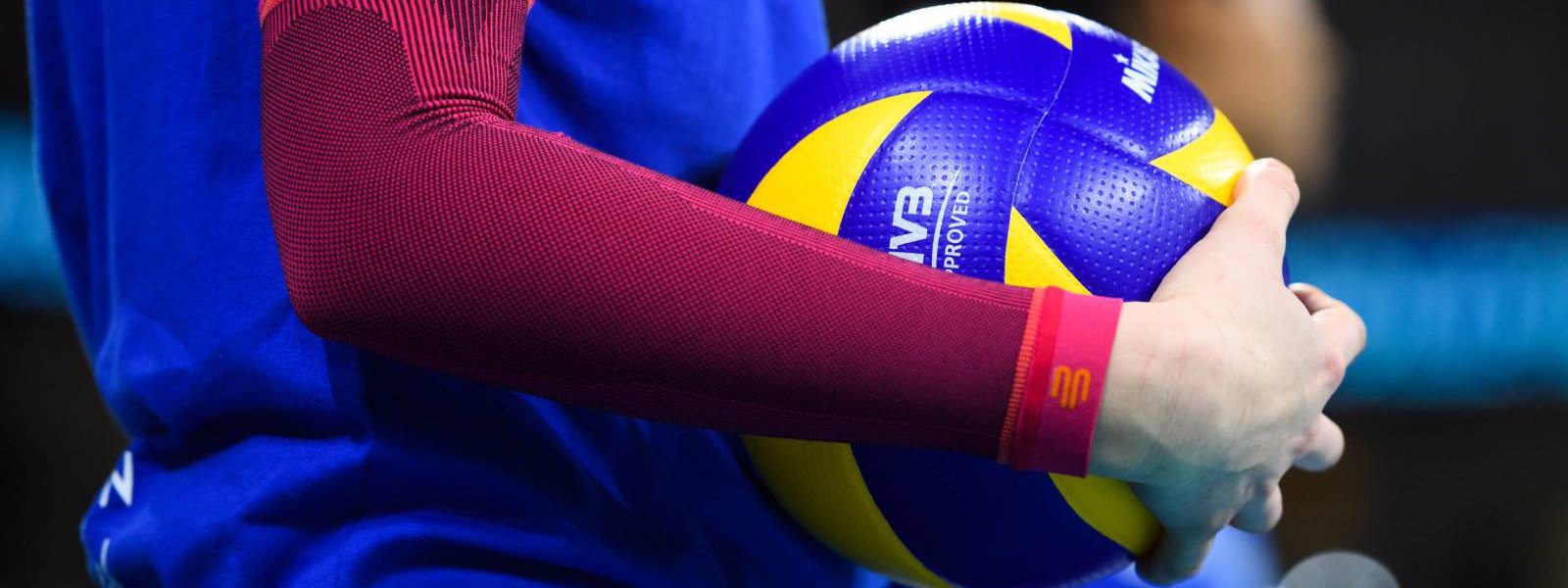 Volleyballspielerin mit pinken Arm Sleeves hat einen Volleyball in der Hand