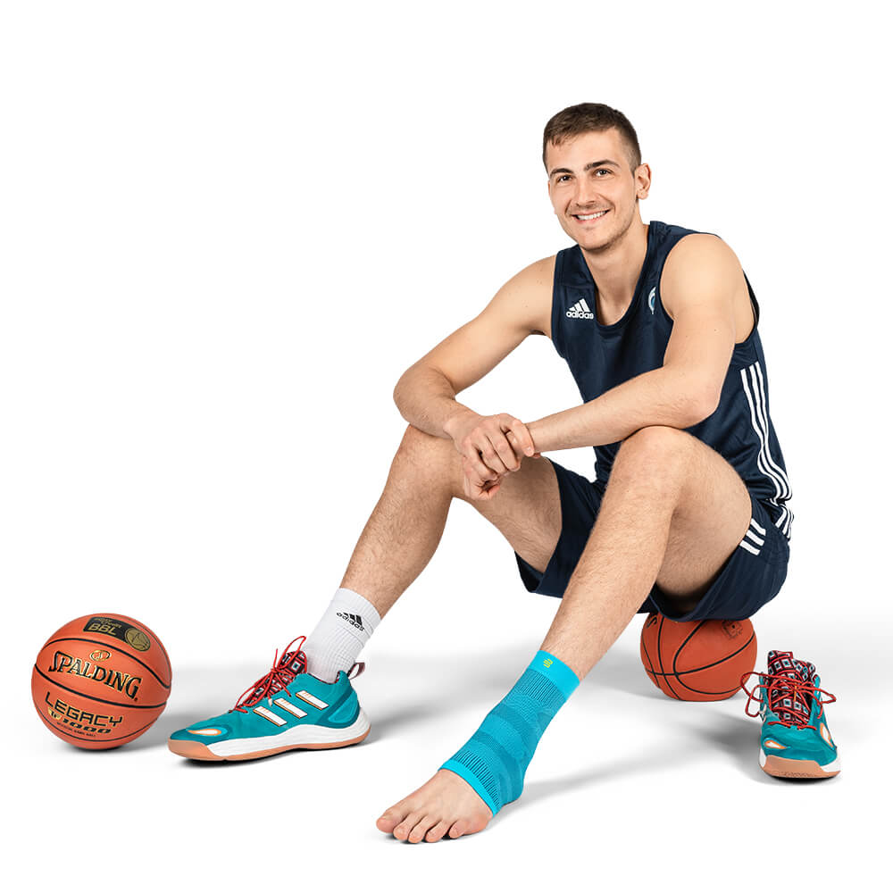 Fußsleeve beim Basketballspielen Spieler sitzt auf einem Basketball mit Sleeve