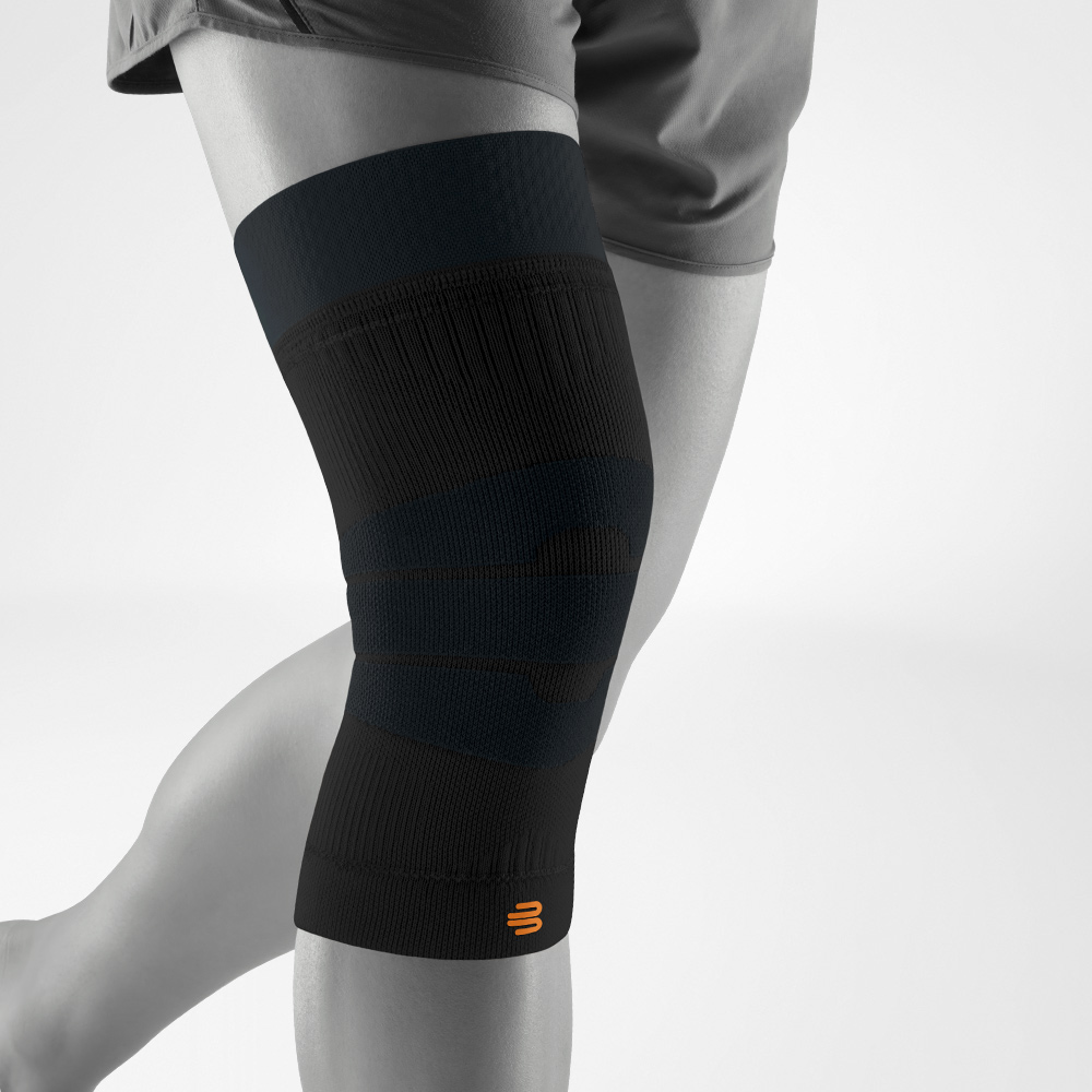 Schwarze Kniebandage in seitlicher Ansicht am Bein getragen. Das flexible Kompressionsgestrick unterstützt das Gelenk bei Outdoor-Bewegungen wie Laufen, Wandern oder Training.