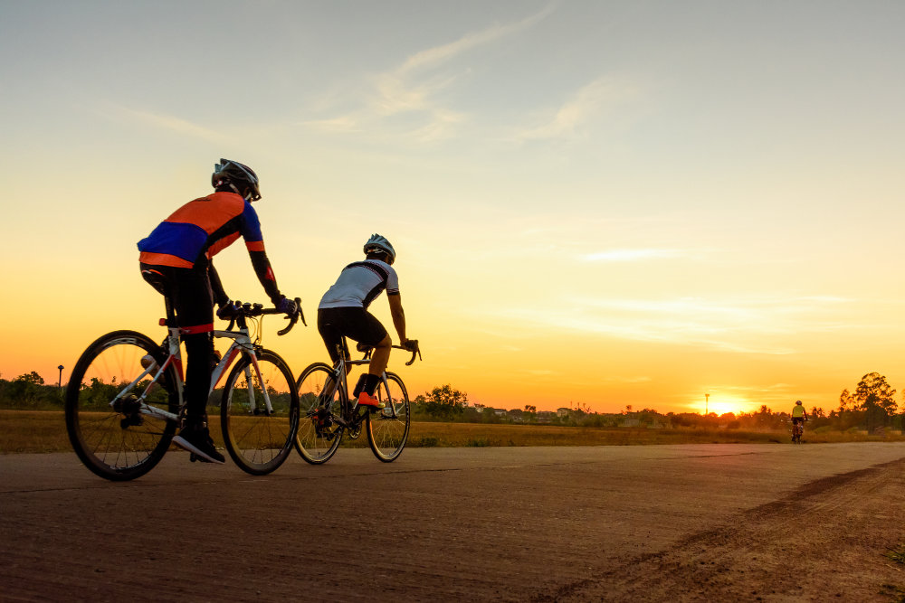 Zwei Rennradfahrer fahren auf einer flachen Betonstraße in den Sonnenuntergang