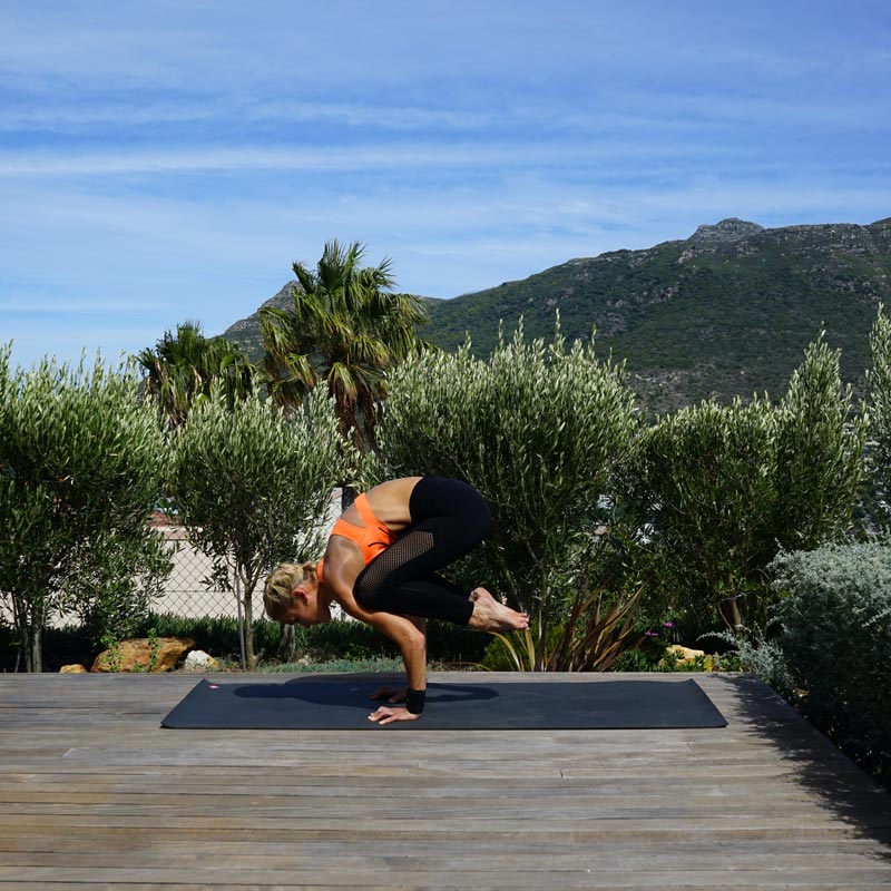 Frau macht Yoga auf ihrer Terrasse	 balanciert auf ihren Händen während ihre Beine hinterm Oberkörper in der Luft hängen