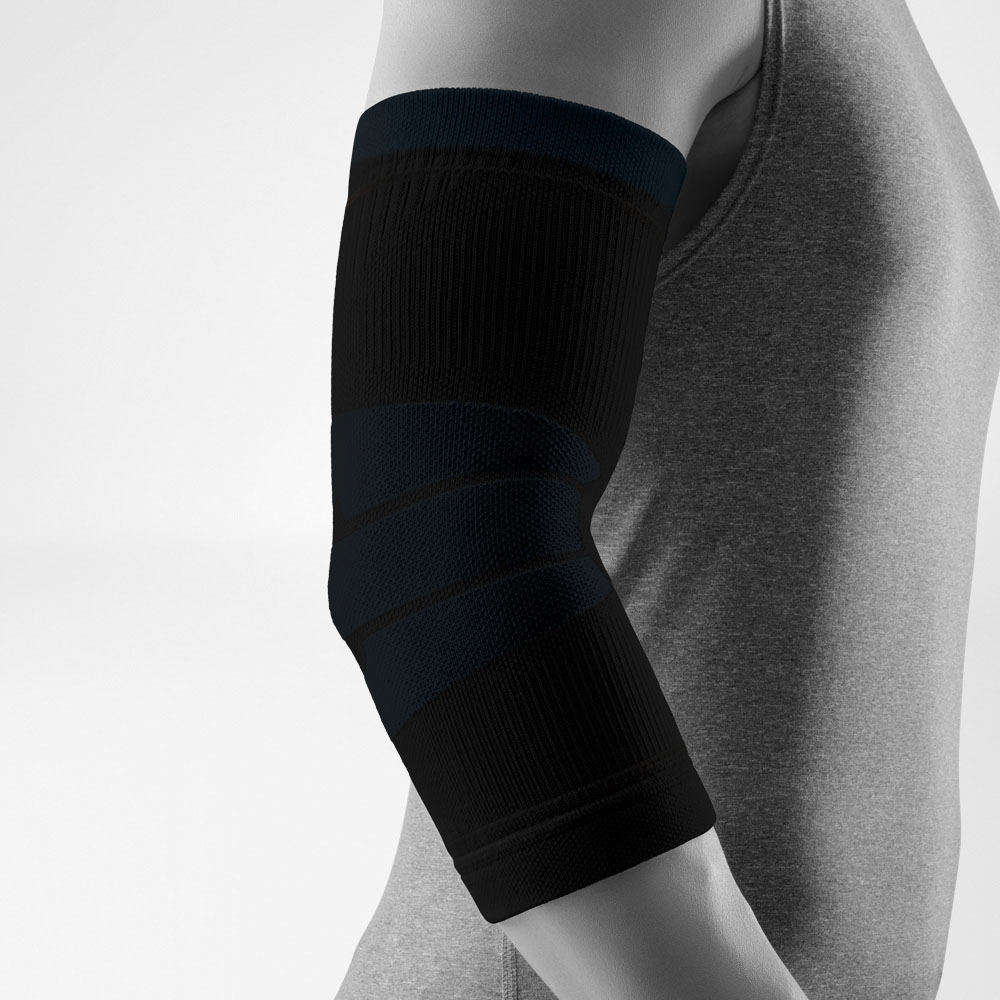 Studioaufnahme eines schwarzen Outdoor Compression Elbow Support am angewinkelten Arm. Die Bandage umschließt den Ellenbogen gleichmäßig, zeigt unterschiedliche Strickzonen und liegt eng an der Haut an. Der Hintergrund ist neutral und hell gehalten.