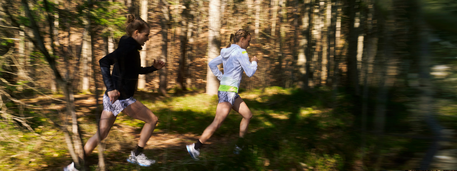 Zwei Läuferinnen laufen schnell durchs Unterholz bei leichter Bildunschärfe