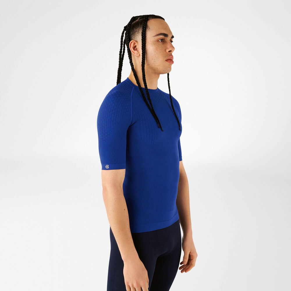 Ein Mann in einem blauen Kompressionsshirt steht seitlich und schaut nach vorne.