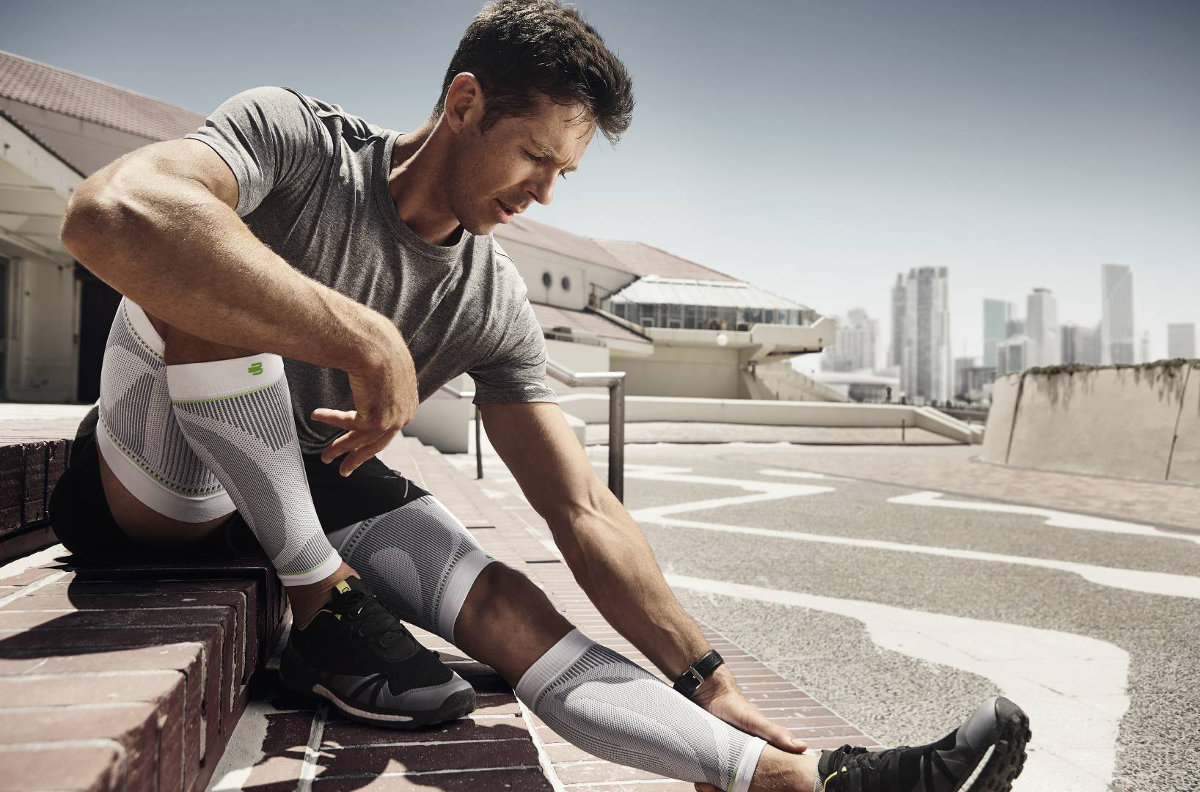 Sports Compression Sleeves Upper und Lower Leg weiß Mann ruht sich auf Stufen im urbanen Umfeld aus und trägt weiße Ober- und Unterschenkel-Sleeves