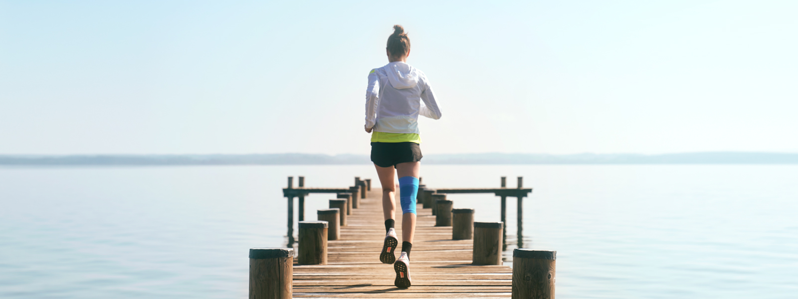 Anna Hahner läuft mit ihre Sports Compression Knee Support über einen Steg in Richtung See