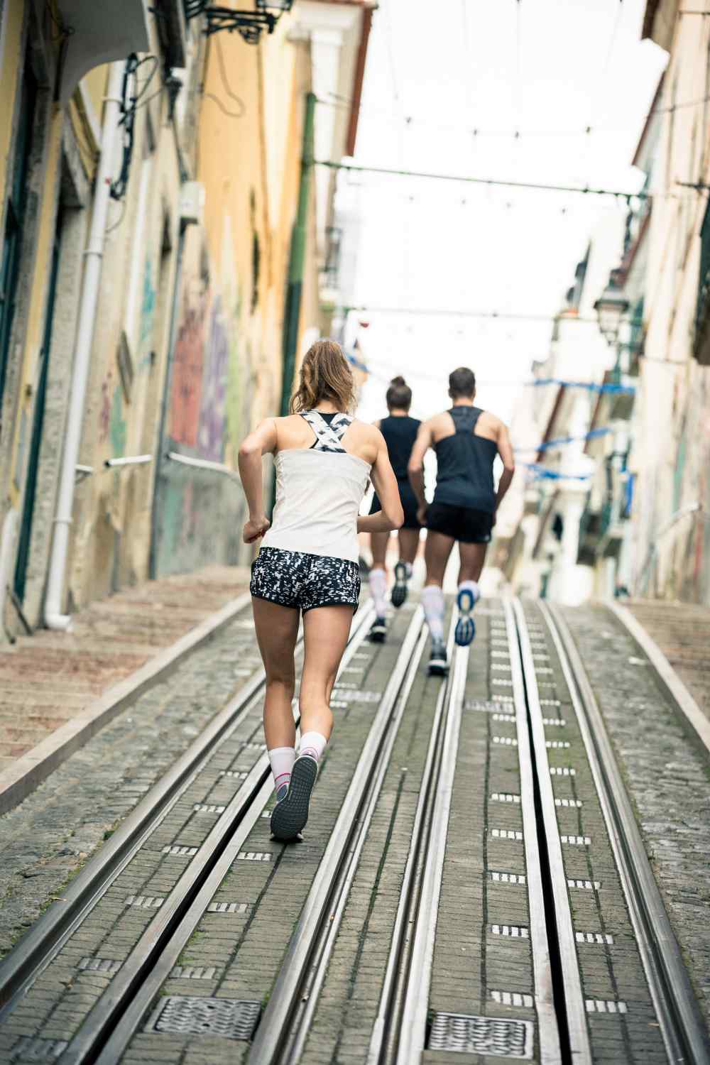 Zwei Läuferinnen und ein Läufer laufen eine Straßenbahnlinie in einer Stadt hinauf
