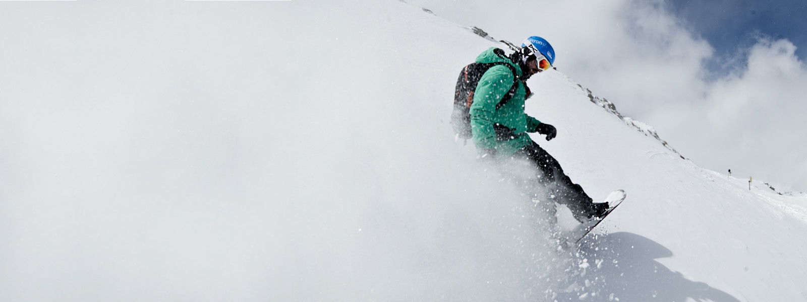Snowboard-Equipment für noch mehr Schwung - hier bei uns Snowboarder mit grüner Jacke wirbelt beim Bremsen Schnee auf	 der die komplette linke Bildseite weiß färbt