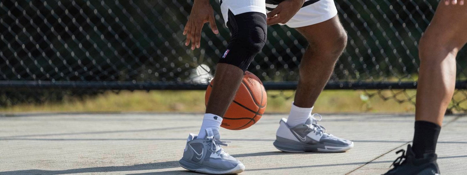 Knee Support NBA beim Basketball Spieler dribbelt auf einem Streetball-Court mit einem Basketball und trägt dabei eine schwarze NBA Knee Support