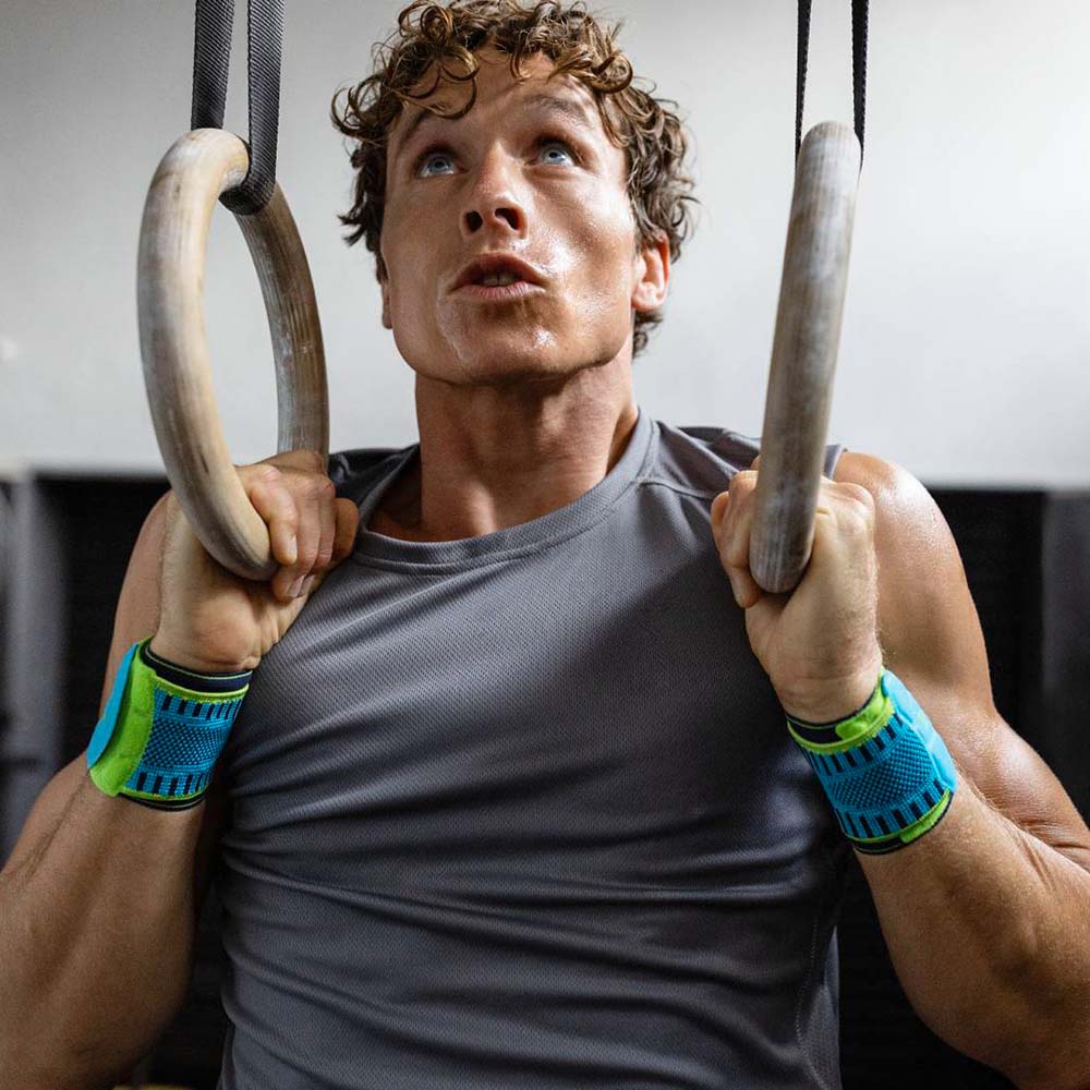 Mann mit Handgelenksbandagen zieht sich an Ringen in einem Fitnessstudio hoch
