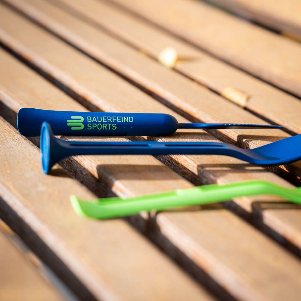 Funktional und stilvoll: Bauerfeind Sports Besteck für Outdoor-Fans Nahaufnahme eines blauen Bestecks auf einer Holzbank, auf dem Griff ist das Logo "Bauerfeind Sports" zu sehen.