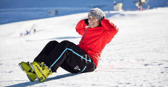 Skiläuferin in roter Jacke macht einen Sit-up im Schnee