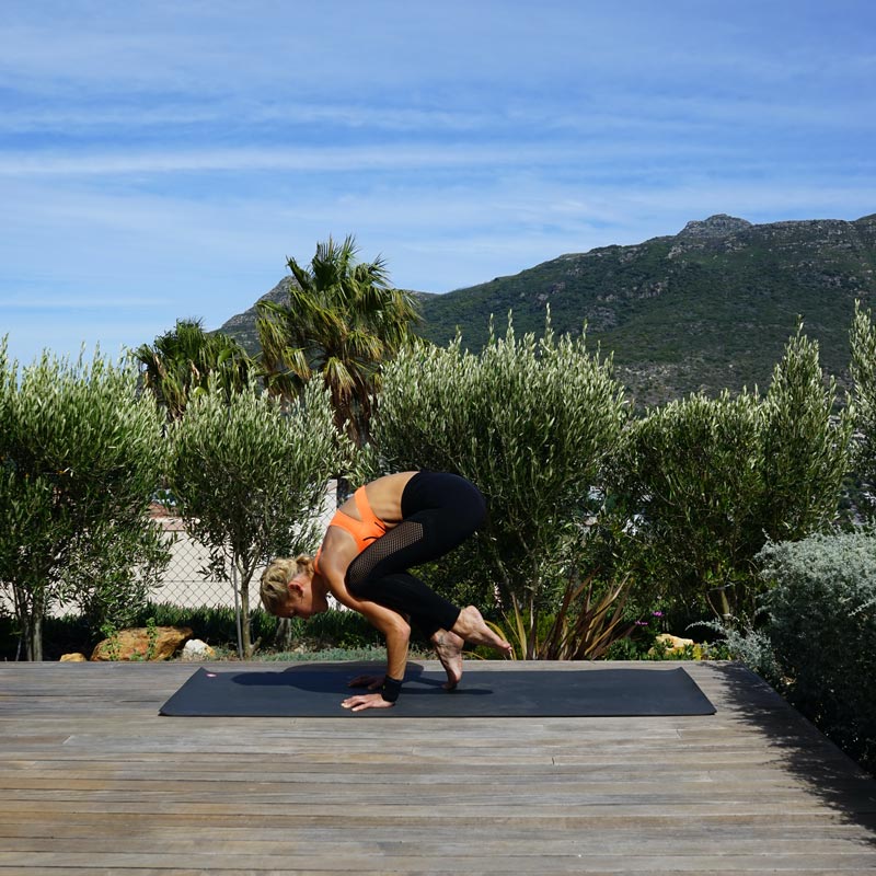 Frau macht Yoga auf ihrer Terrasse	 balanciert auf ihren Händen während ihre Beine sich langsam vom Boden in die Luft heben