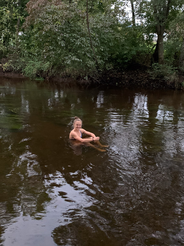 Hahner im kalten Flusswasser Anna Hahner im Fluss, von Bäumen umgeben, lächelnd und in die Kamera schauend.