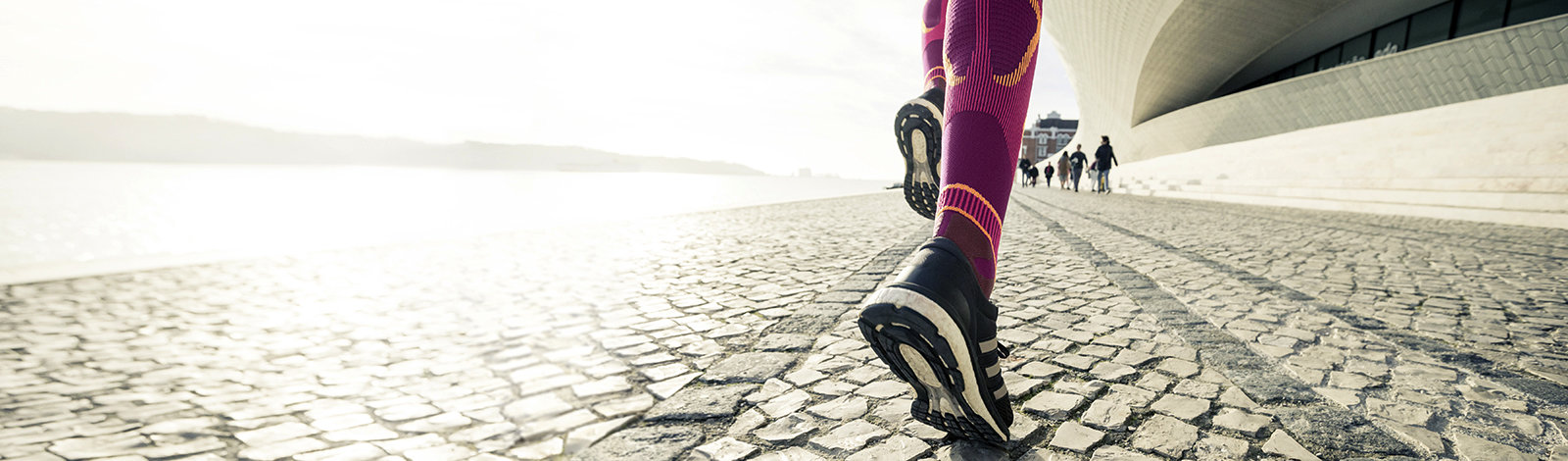 Nahaufnahme: Lange pinke Laufsocken und schwarze Laufschuhe laufen über eine gepflasterte Straße in einer Stadt