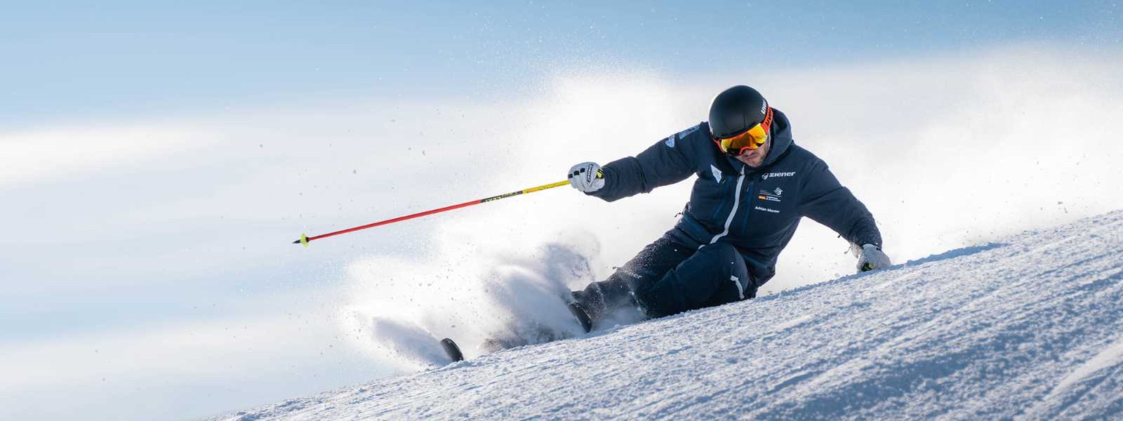Skifahrer in dunklem Anzug in extremer Schräglage bei der Abfahrt